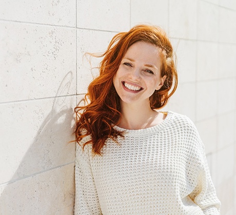 Red-haired woman in white sweater leaning on wall