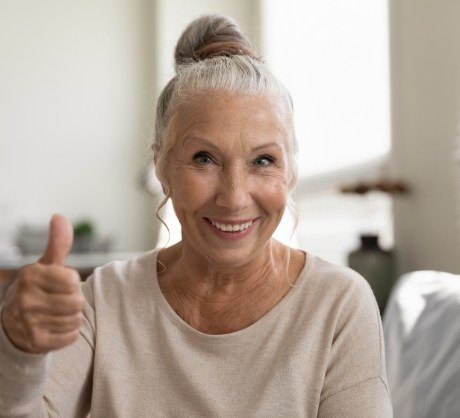 Woman with healthy smile giving thumbs up after dental office visit