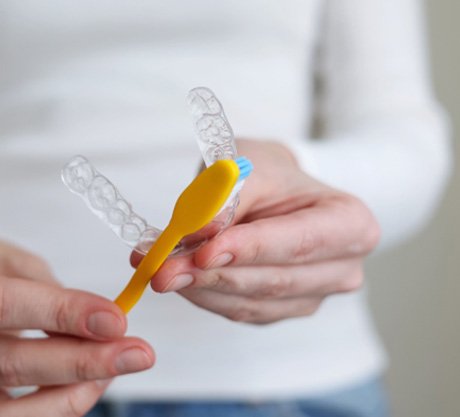 Patient using yellow toothbrush to clean their aligners  