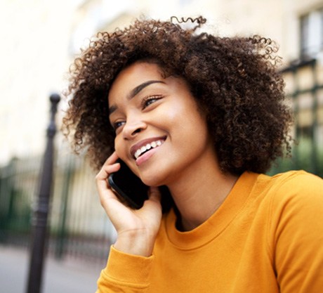 Woman in orange shirt smiling on the phone outside 